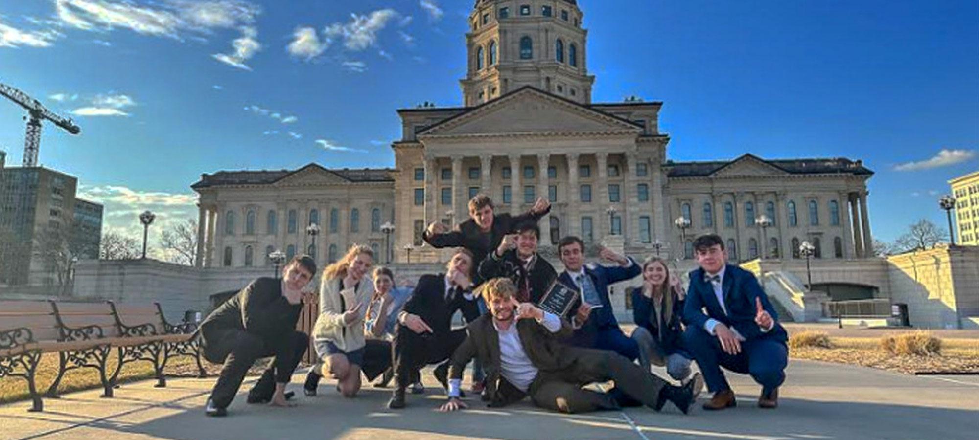 Students doing a fun group pose in front of the building